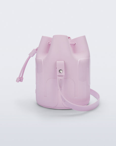 Side view of a Melissa Station bucket bag in Light Pink. The bag has an adjustable shoulder strap and a drawstring top closure.
