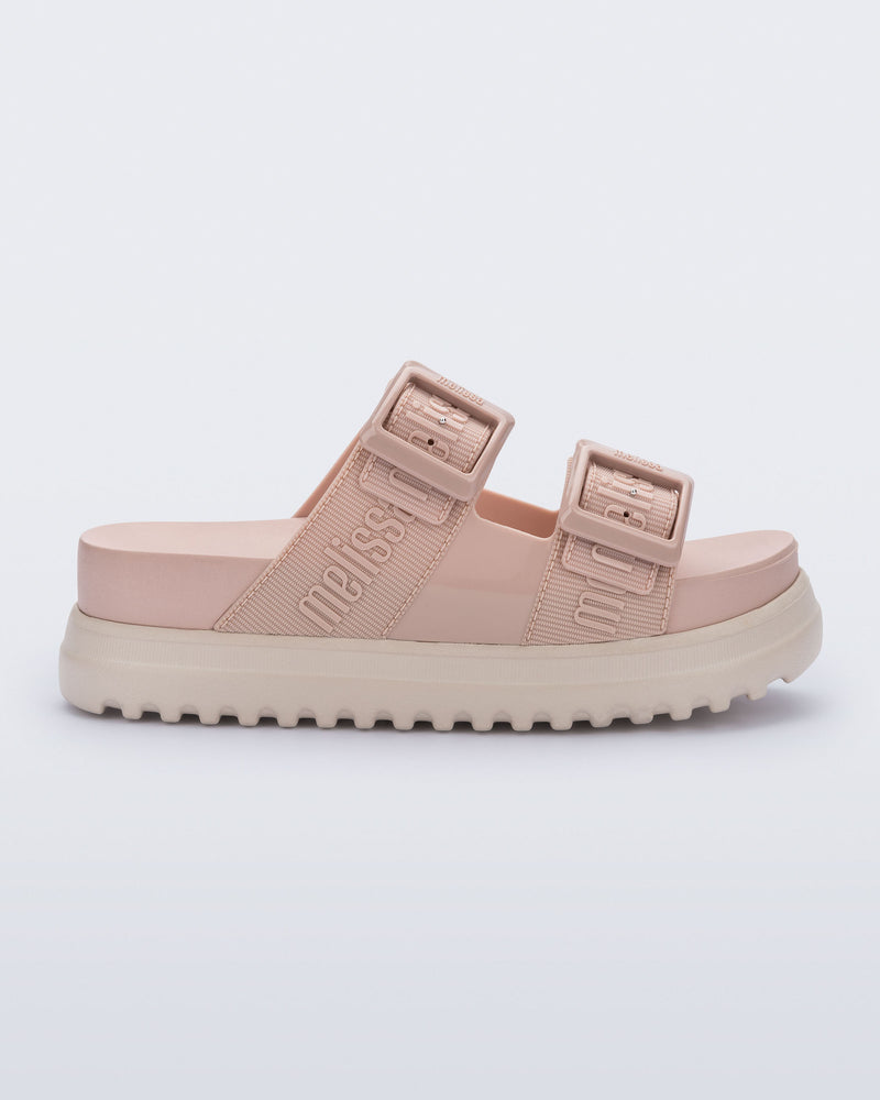 Side view of the melissa cozy platform slide sandal. There are two buckle straps that go across the foot with the M Lover (melissa logo) print embossed into the straps. The buckles are located on the outside edge of the two straps. The straps and insole of the shoe are light pink and the platform sole is beige.