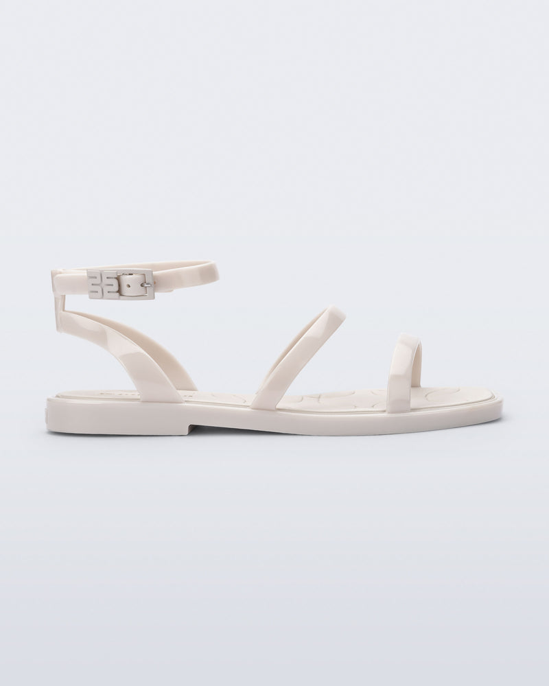 Side view of the Melissa Heat Sandal. This is a flat sandal with a multiple straps, one across the toes, mid part of the foot, and a buckle strap around the ankle with a supporting strap that connects the ankle strap to the sole of the shoe. The straps, insole, outsole, and buckles on the ankle strap are beige. The insole is embossed with a geometric pattern.