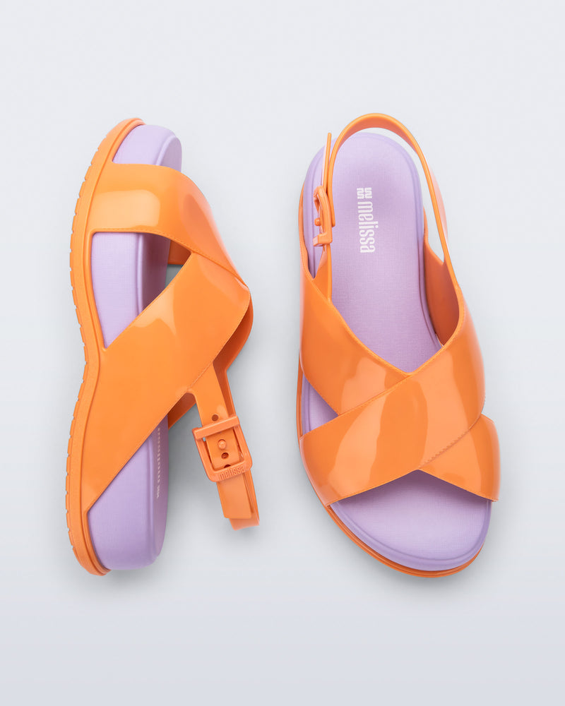 Top and side view of a pair of Melissa Mare platform sandals. This sandal has two cross straps across the front part of the foot with a thin buckle strap attached. The straps and outsole are orange whiles the platform insole is purple.