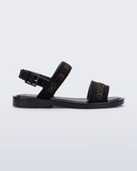 Side view of the Melissa Mar Sandal with Melissa logo embossed into the straps. There are two embossed straps that go across the foot; 1 across the toes and the other across the main part of the foot. The main foot strap has an ankle strap attached with a buckle closure. The straps ,buckle and sole of the shoe is black. The Melissa logo on the straps has a black metallic finish. . The buckle placement is on the outside of the ankle strap.