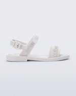 Side view of the Melissa Mar Sandal with Melissa logo embossed into the straps. There are two embossed straps that go across the foot; 1 across the toes and the other across the main part of the foot. The main foot strap has an ankle strap attached with a buckle closure. The straps ,buckle and sole of the shoe is white. The Melissa logo on the straps has a silver metallic finish. . The buckle placement is on the outside of the ankle strap.