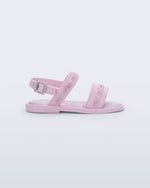 Side view of the Mini Melissa Mar Sandal with Mini Melissa logo embossed into the straps. There are two embossed straps that go across the foot; 1 across the toes and the other across the main part of the foot. The main foot strap has an ankle strap attached with a buckle closure. The straps ,buckle and sole of the shoe is pink. The Melissa logo on the straps has a silver metallic finish. . The buckle placement is on the outside of the ankle strap.