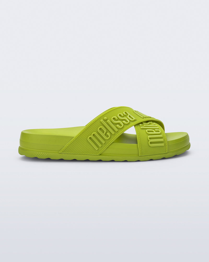 Side view of the Melissa Cozy slide sandals. The slide has two cross straps with Melissa logo embossed onto the straps. The color of the shoe is a lime green.