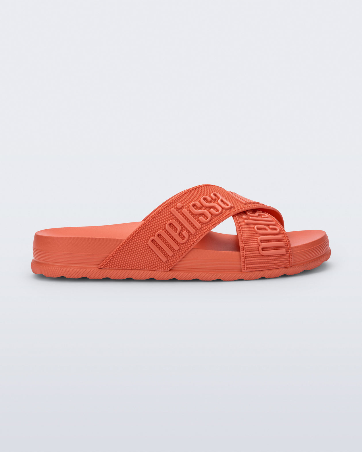 Side view of the Melissa Cozy slide sandals. The slide has two cross straps with Melissa logo embossed onto the straps. The color of the shoe is orange.