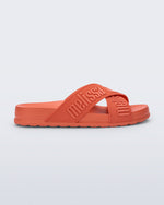 Side view of the Melissa Cozy slide sandals. The slide has two cross straps with Melissa logo embossed onto the straps. The color of the shoe is orange.