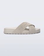 Side view of the Melissa Cozy slide sandals. The slide has two cross straps with Melissa logo embossed onto the straps. The color of the shoe is beige.