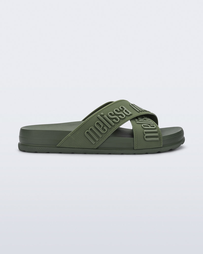 Side view of the Melissa Cozy slide sandals. The slide has two cross straps with Melissa logo embossed onto the straps. The color of the shoe is a dark green.