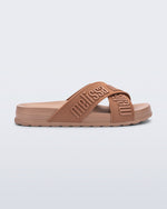 Side view of the Melissa Cozy slide sandals. The slide has two cross straps with Melissa logo embossed onto the straps. The color of the shoe is brown.