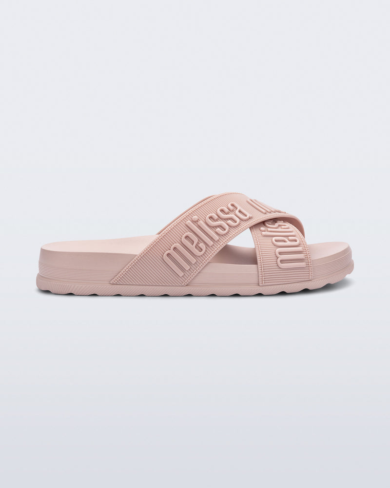 Side view of the Melissa Cozy slide sandals. The slide has two cross straps with Melissa logo embossed onto the straps. The color of the shoe is light pink.