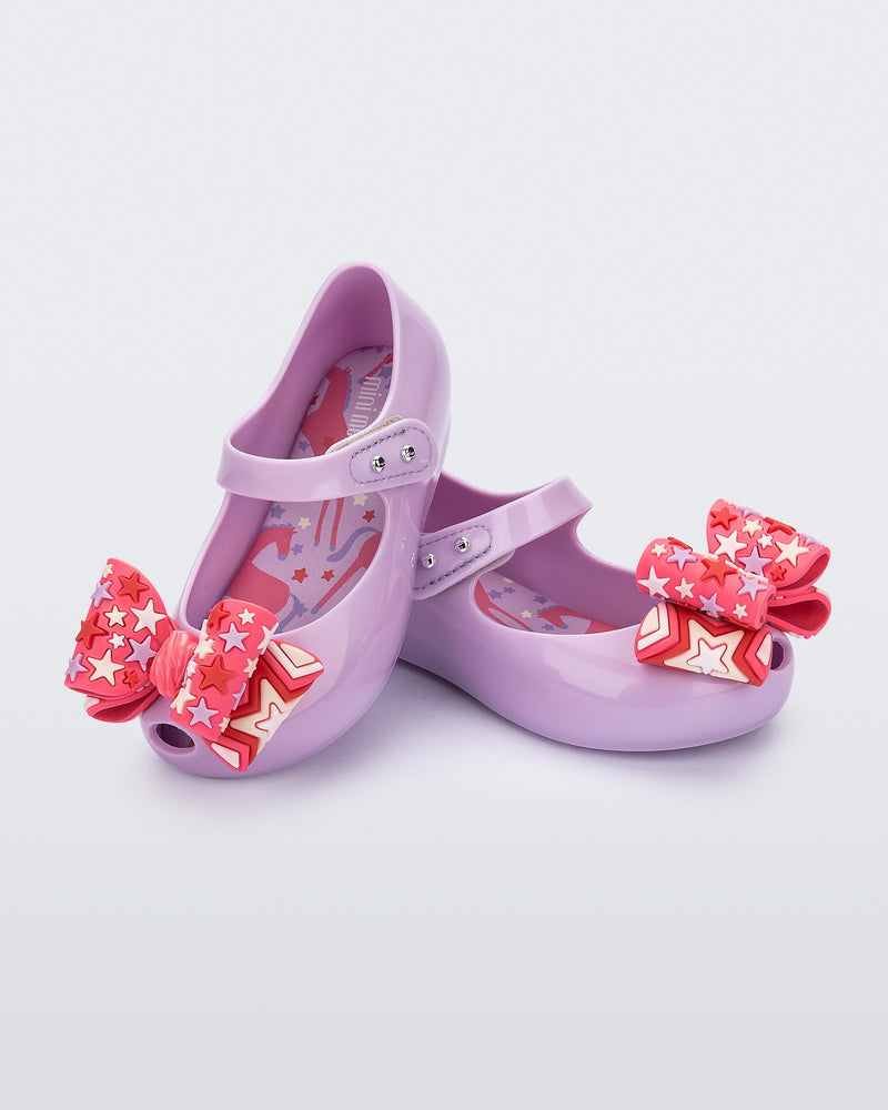 Angled view of a pair of lilac with pink star patterned bow Ultragirl Wonderland baby flats