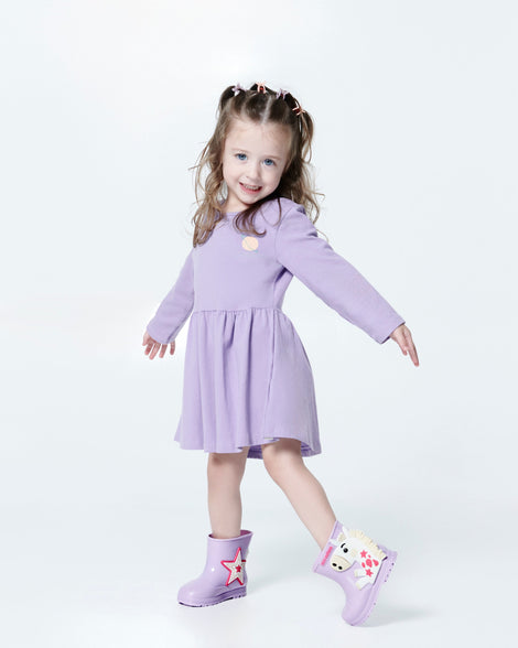 Child model in a lilac dress wearing a pair of lilac Welly Wonderland baby boots with white pony on one shoe and star on the other