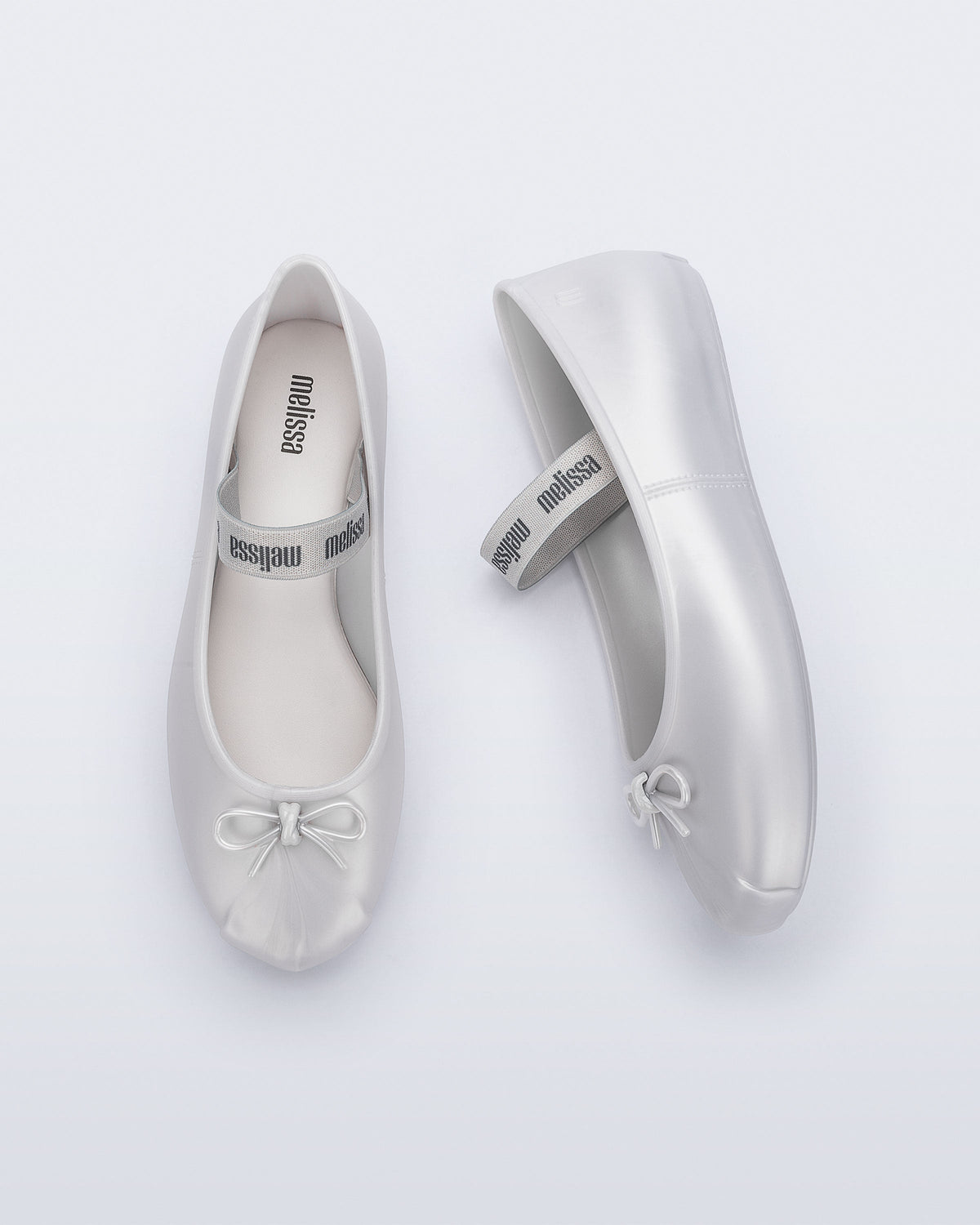 Side and top view of a pair of pearly white Sophie flats with top elastic strap and small bow