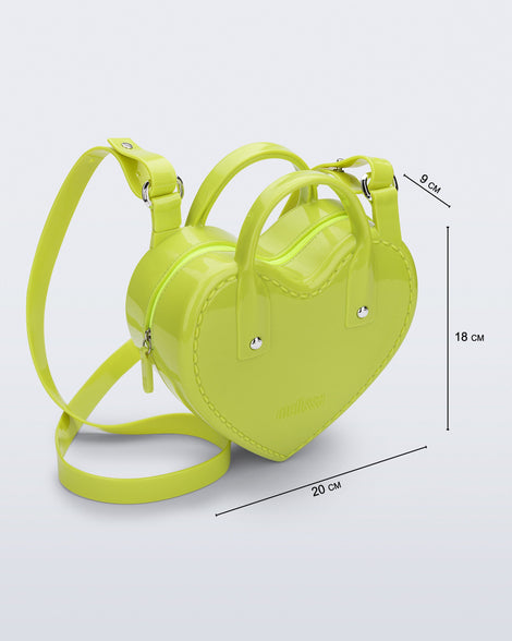 Angled view of a green Heartbeat bag with small handles and longer strap and bag dimensions: 20cm x 9cm x 18 cm.