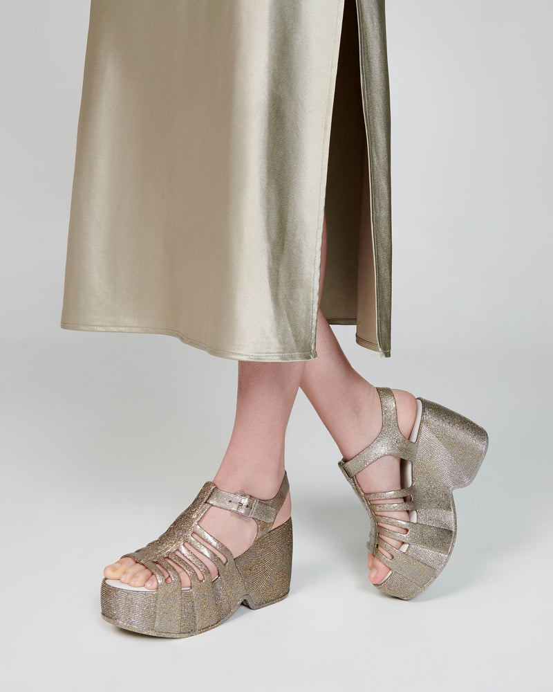 Model's legs wearing a pair of glitter gold Station 79 platform heels with ankle strap