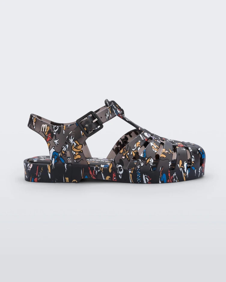 Side view of a Mini Melissa Possession fisherman sandal in black with all over Disney character print. There is a buckle closure on the side of the ankle strap.