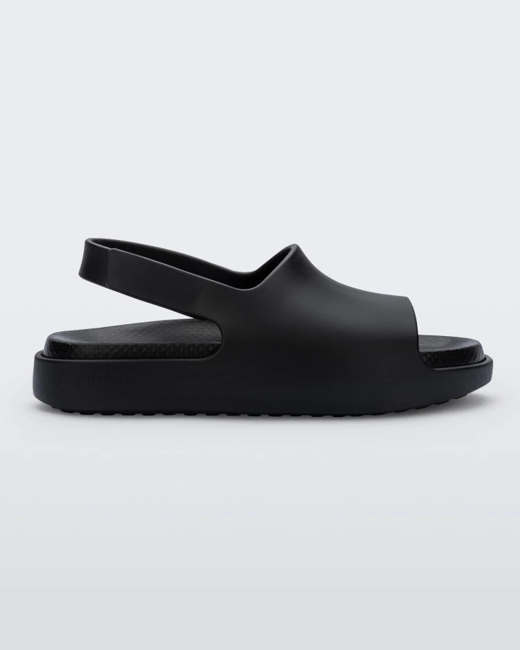 Side view of a matte black Mini Melissa Cloud sandal with a black insole, base and back velcro strap.