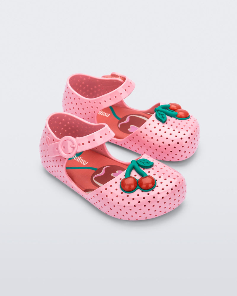 Angled view of a pair of pink Pop baby flats with two red cherries