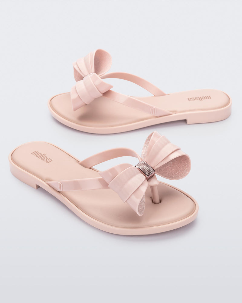 Angled view of a pair of Melissa slim strap flip flops in glitter pink with bow applique