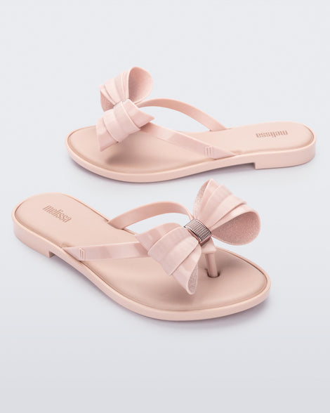Angled view of a pair of Melissa slim strap flip flops in glitter pink with bow applique