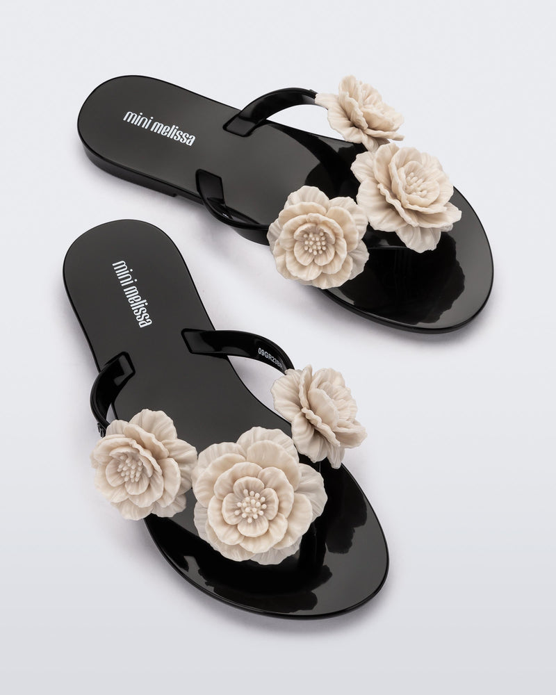 Top view of a pair of a black Harmonic Springtime kids flip flop with three beige flowers.