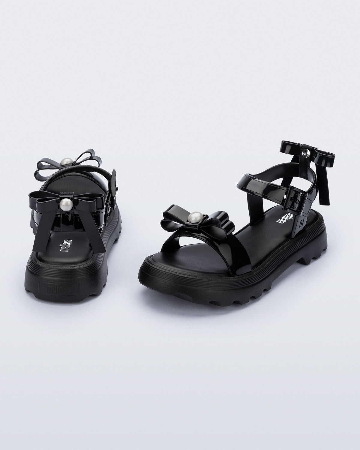 Angled and back view of a pair of black Town Bow sandals with bows and a pearl in the center of each bow