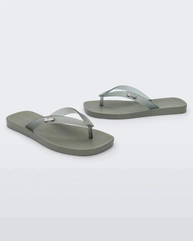 An angled front and side view of a pair of green/clear Melissa Sun Long Beach flip flops with a green base and clear green straps with "melissa" on the strap.