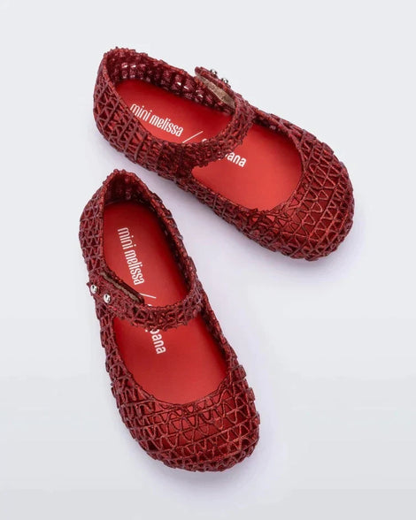 A top view of a pair of red glitter Mini Melissa Campana flats with a snap strap for baby and an open woven texture.