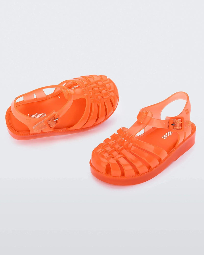 An angled front and side view of a pair of orange Mini Melissa Possession sandals with several straps, a closed toe front and a back ankle strap.