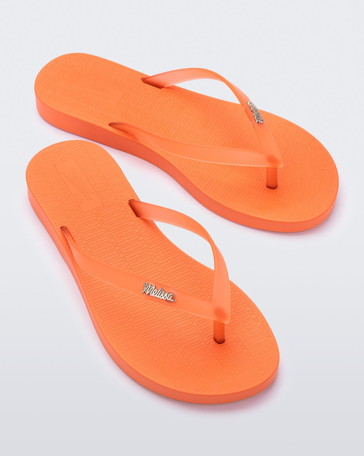 An angled top view of a pair of orange Melissa Sun Venice flip flops with "melissa" on the strap.