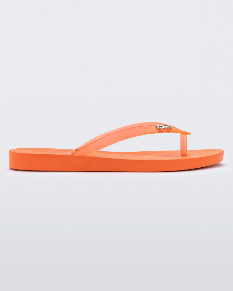 An outter side view of an orange Melissa Sun Venice flip flop with "melissa" on the strap.