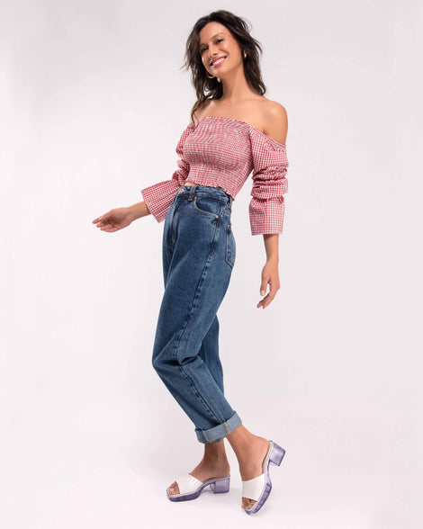 A model's posing in jeans and a red and white checkered top is wearing a pair of Melissa Shape slides with clear heel and white wide strap
