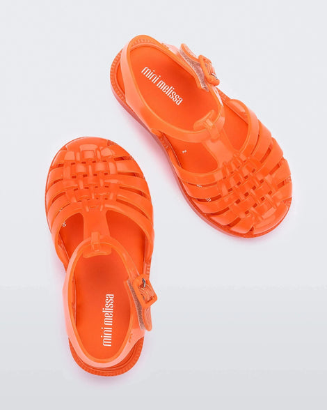 A top view of a pair of orange Mini Melissa Possession sandals with several straps, a closed toe front and a back ankle strap.
