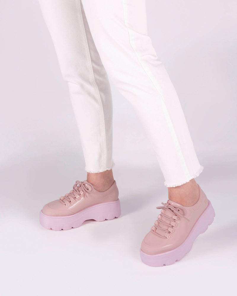 A model's legs wearing white jeans and a pair of pink platform Melissa Kick Off Sneaker with laces.