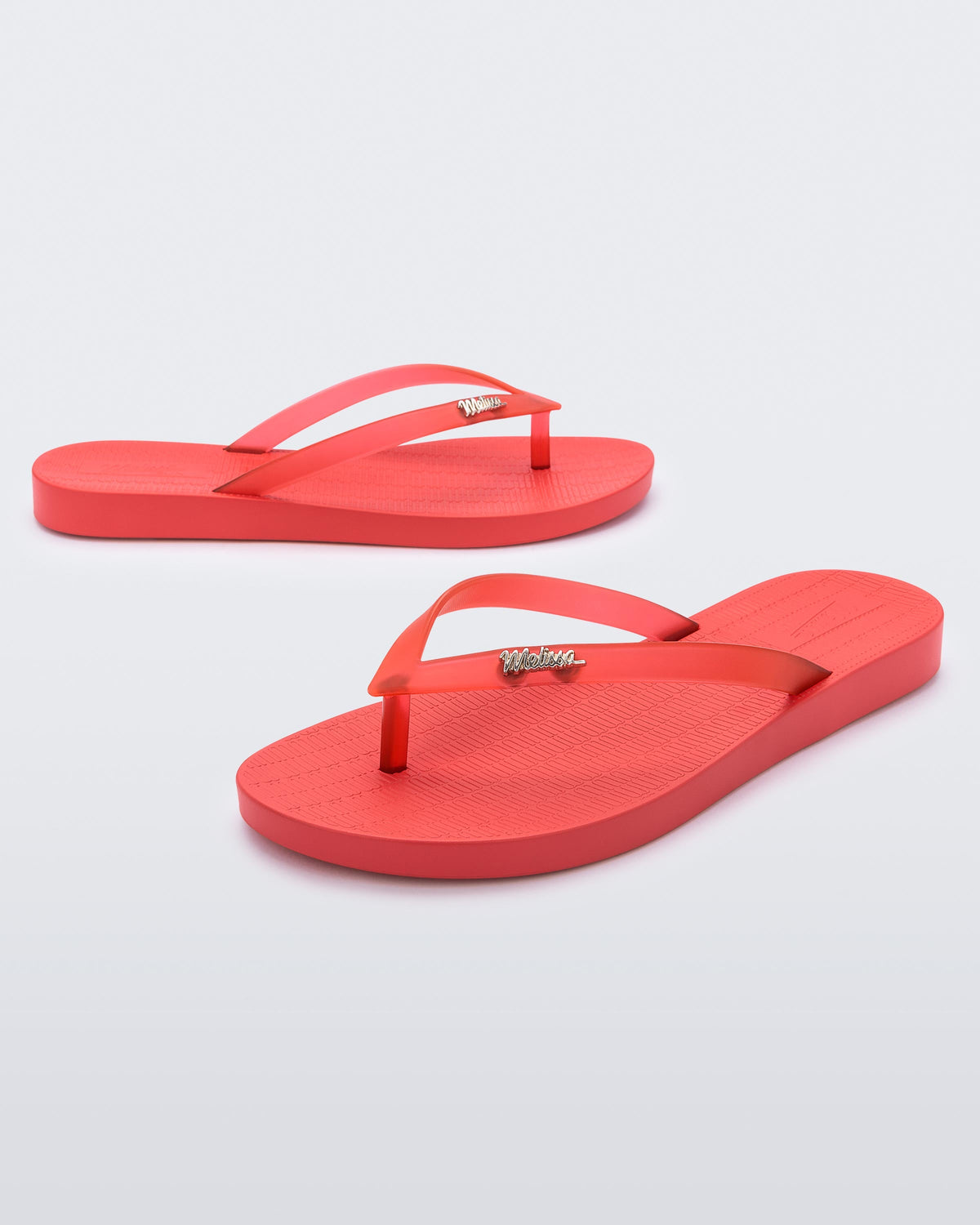 A front and side view of a pair of red Melissa Sun Venice flip flops with a "melissa" logo on the strap.