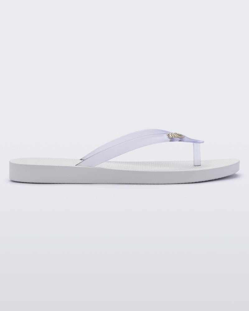 An outter side view of a white/clear Melissa Sun Venice flip flop with a white sole and clear straps with "melissa" on one strap.