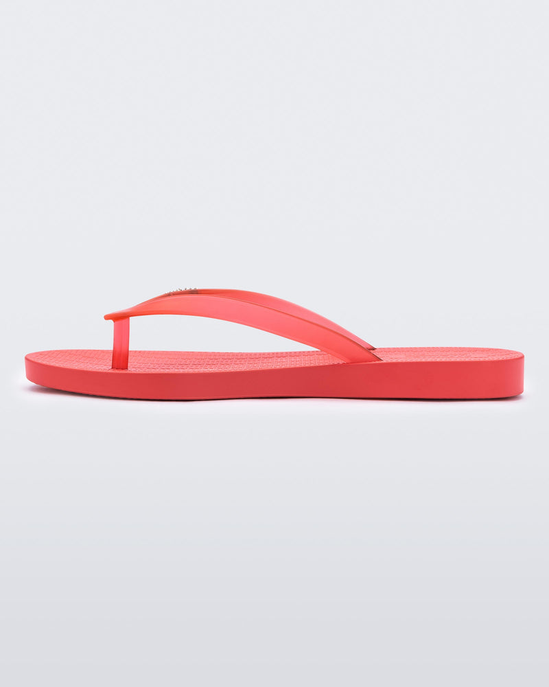 An inner side view of a red Melissa Sun Venice flip flop with a "melissa" logo on the strap.