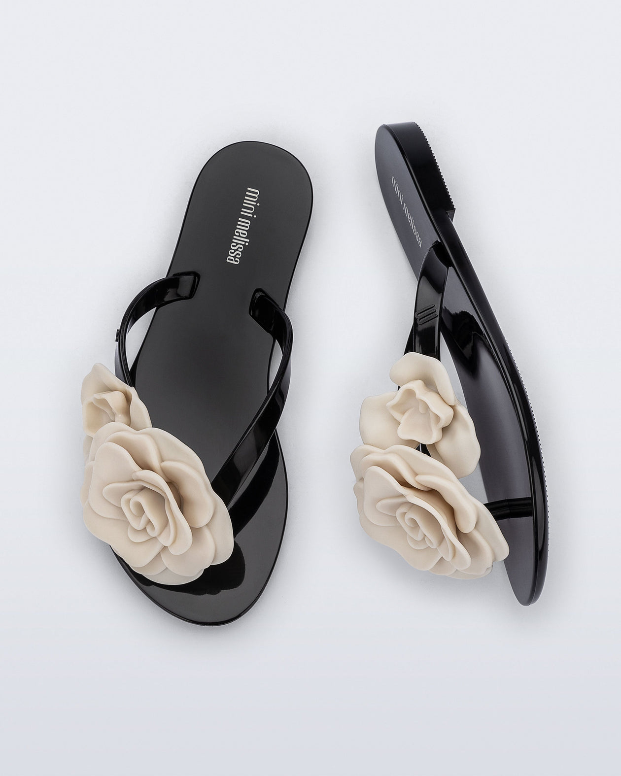 Top and side view of a pair of black Harmonic Petals kids flip flops with beige flowers