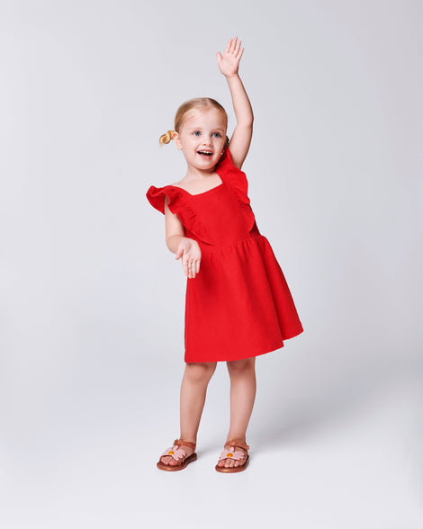 Child model in a red dress wearing a pair of pearly brown baby Hip Bloomy sandal with pink flower