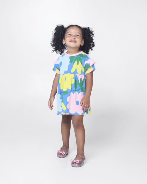 A model posing for a picture in a blue patterned dress and a pair of Glitter Pink Mini Melissa Ultragirl Bow flats with a pink glitter base, top strap and pink bow on the toe.