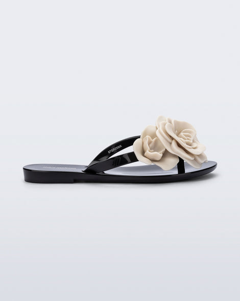 Side view of a black Harmonic Petals kids flip flop with beige flowers