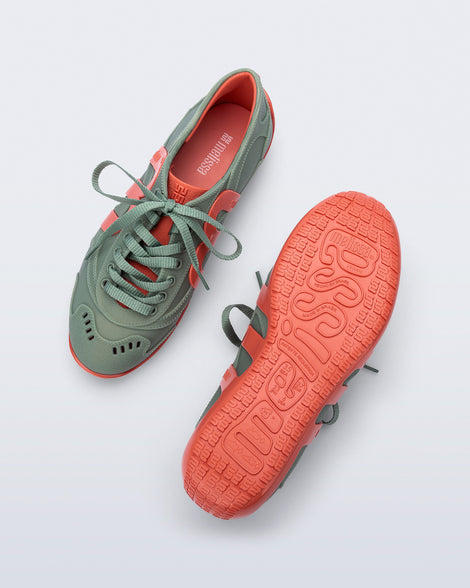 Top and bottom view of a pair of green Motion sneakers with orange colored sole and M monogram on side