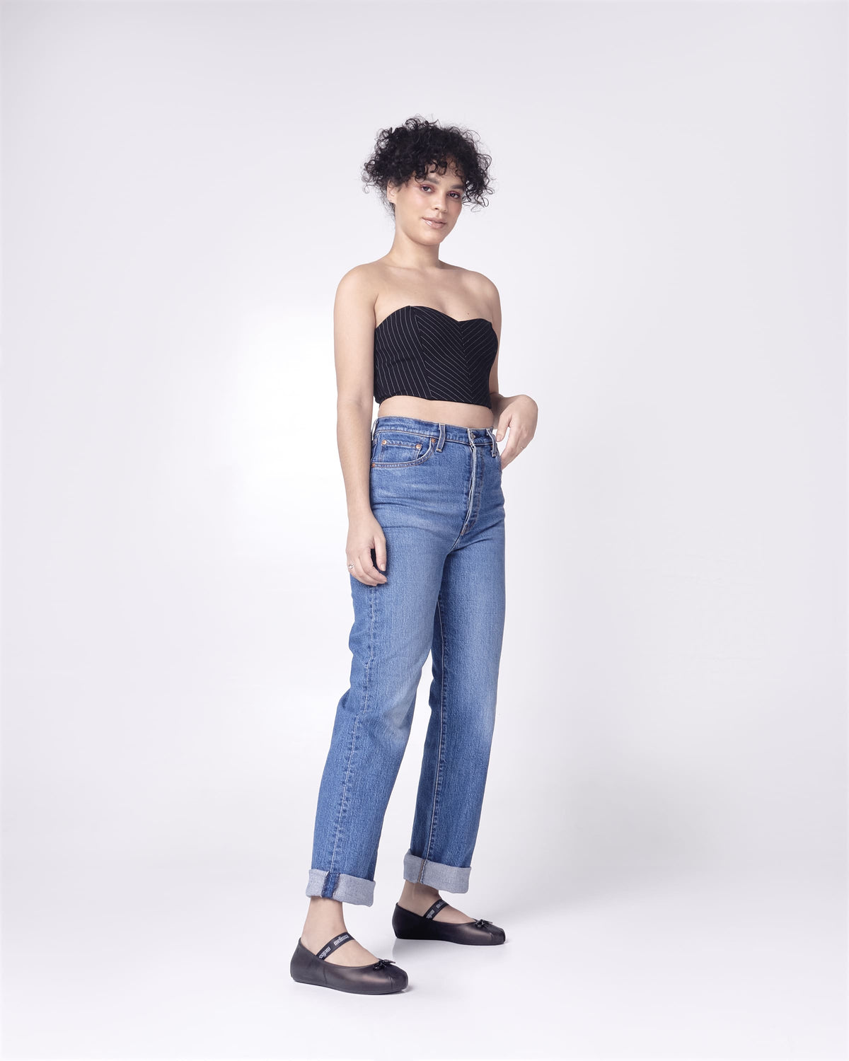 Model posing in jeans and a black top wearing a pair of Melissa Sophie ballet flats in black with M-logo strap and bow applique