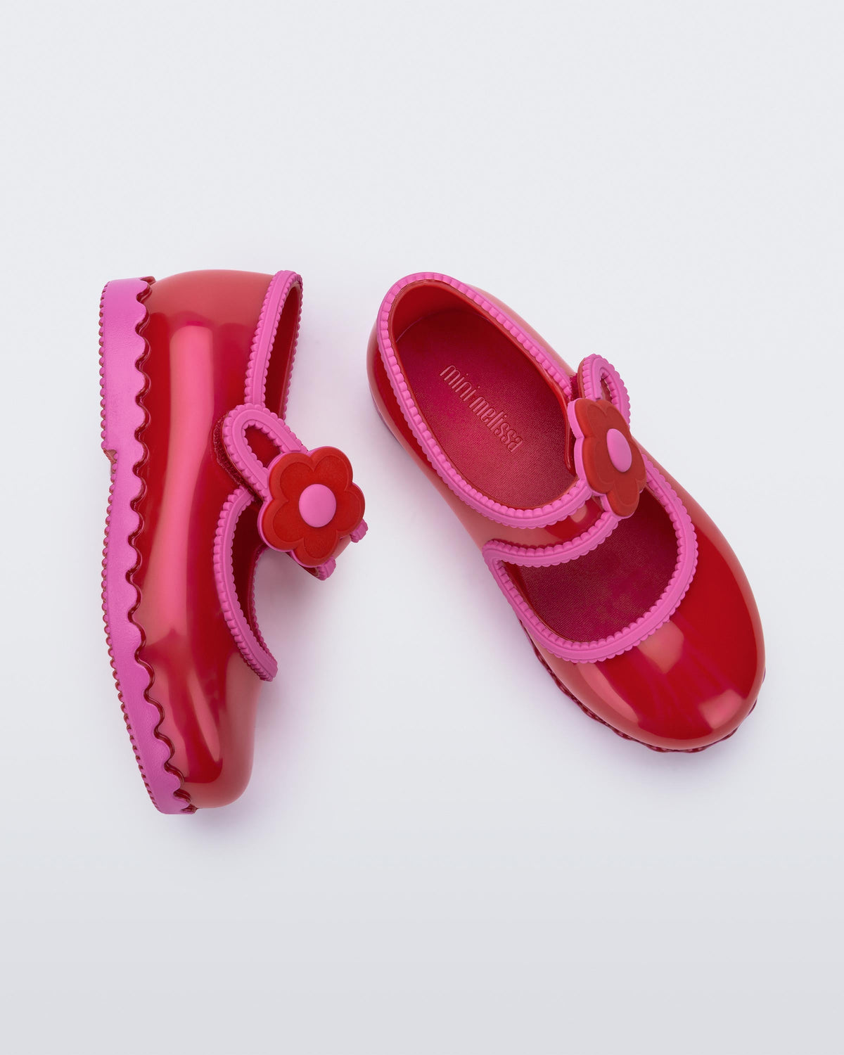Side and top view of a pair of red with pink trim Hip Ballerina baby flats with strap with flower