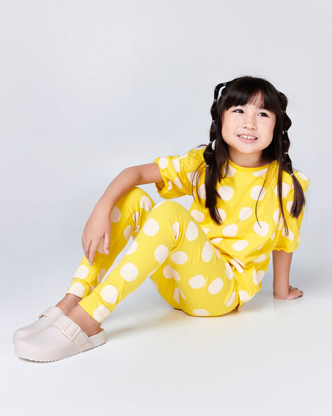 Child model in a yellow outfit wearing a pair of beige kids Cozy Clogs