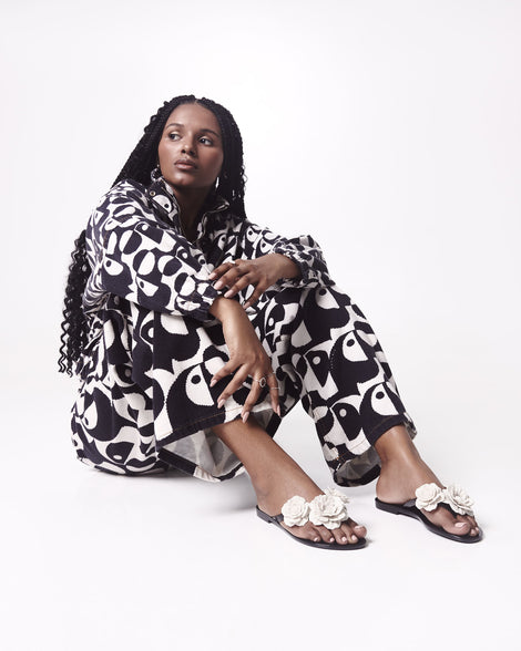Model in a black and white outfit wearing a pair of a black Harmonic Springtime women's flip flop with 3 beige flowers