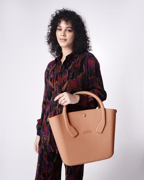 Model in a black patterned outfit holding by the handles a brown Free Big Bag