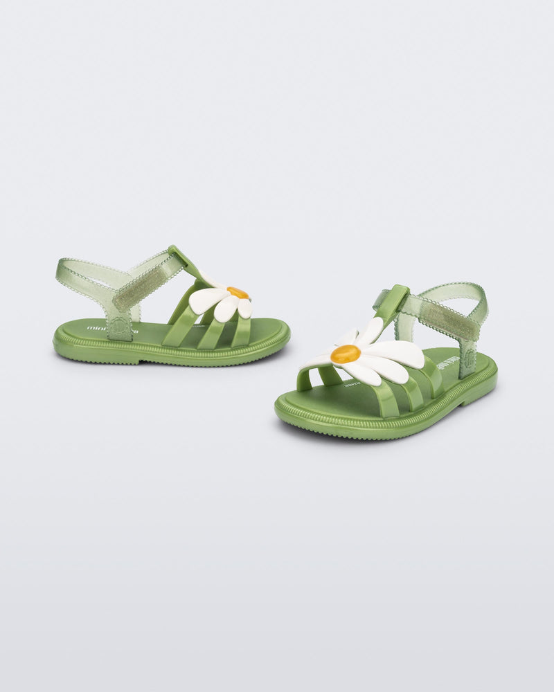 Angled view of a pair of green baby Hip Bloomy sandal with a white flower