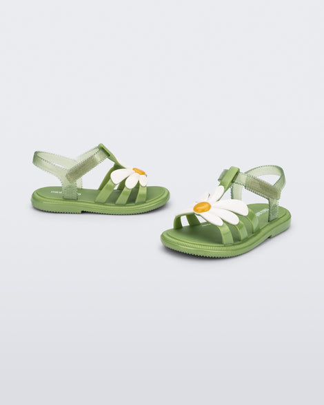 Angled view of a pair of green baby Hip Bloomy sandal with a white flower