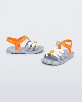 Angled view of a pair of blue baby Hip Bloomy sandal with orange strap and white flower